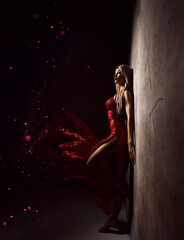 Romantic girl in long tight red dress stands at concrete wall dreaming over dark with stars sparkle. Magic. Miracle