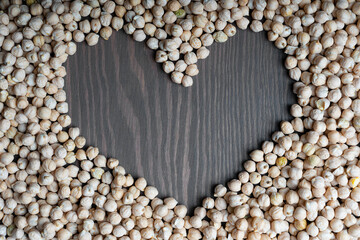 Uncooked raw chickpeas laying on dark wooden surface and forming heart shaped frame. Image with copy space, horizontal orientation. Chickpea is useful for vegan diet as meat analog