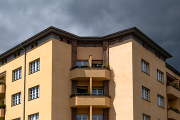 Fototapeta na wymiar Deunkle Gewitterwolken über einem von der Sonne beschienenem Wohnhaus an der Wisbyer Strasse in Berlin