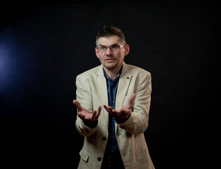 mature actor in glasses and classic jacket looks straight and stretches hands ahead playing role at etude audition closeup