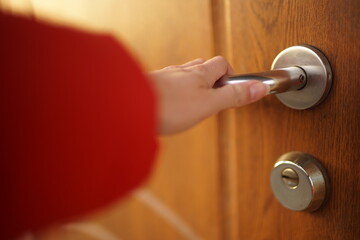 Female hand opens a brown wooden door by clicking on a chromed handle outdoors.