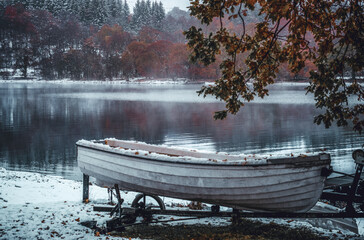 Snow dusted white boat with autumnal winter background scene and glossy reflective lake.