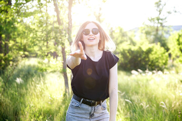 a beautiful girl in sunglasses, a black T-shirt, shades her hand to the camera, the glare of the...