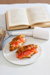 Delicious breakfast with croissant, smoked salmon, cheese and pepper on white plate. Opened old book on the background.
