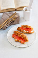 Delicious breakfast with croissant, smoked salmon, cheese and pepper on white plate. Opened old book on the background.