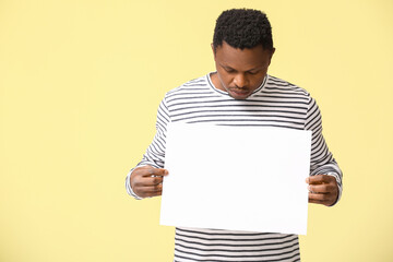 Sad African-American man with poster on color background. Stop racism