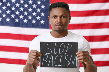 Sad African-American man with poster near national flag of USA. Stop racism