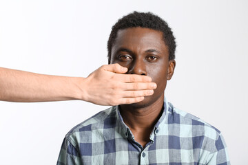 Person covering mouth of sad African-American man on light background. Stop racism