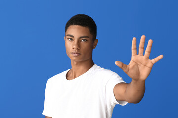 Sad African-American teenage boy showing stop gesture on color background. Stop racism