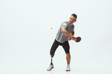 Plakat Athlete with disabilities or amputee isolated on white studio background. Professional male table tennis player with leg prosthesis training in studio. Disabled sport and healthy lifestyle concept.
