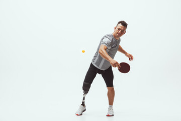 Athlete with disabilities or amputee isolated on white studio background. Professional male table tennis player with leg prosthesis training in studio. Disabled sport and healthy lifestyle concept.