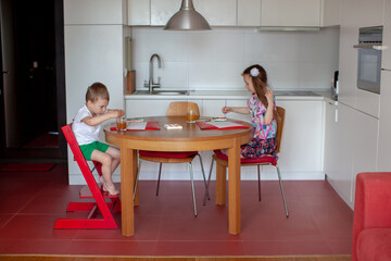 Seven year old girl and three year old boy paint in the kitchen. Modern home interior with white and red colors. 