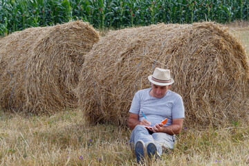 Naklejka na ściany i meble Farmer Writing in Notebook While leaning on Bale of Straw