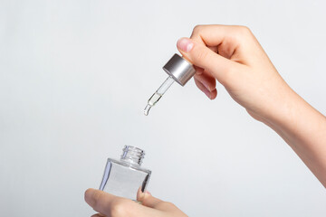 Pipette dropper with drop of natural oil above glass bottle on white background. Natural organic skin care beauty products.