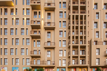 Sand color facade of modern residenial building, with rows of small windows and balconies, front view.