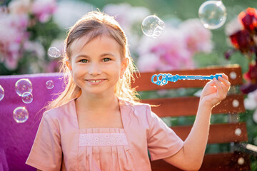 girl blows soap bubbles on the background of flowers in the garden