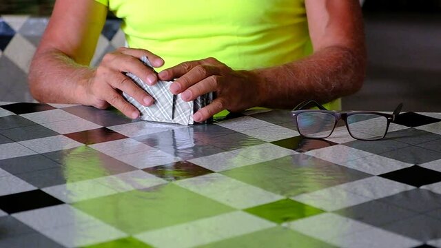 A man in a yellow T-shirt shuffles a deck of playing cards. Tanned hands over the table are warming up before the game. Summer. Georgia. Day.