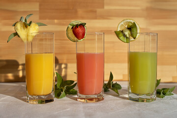 High glass glasses with juice and pieces of fruit on the edge of the glass pineapple, strawberry, kiwi. Healthy lifestyle, refreshing healthy soft drinks