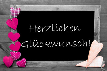 Balckboard With German Text Herzlichen Glueckwunsch Means Congratulations. Gray Wooden Background With Colored Pink Heart Decoration