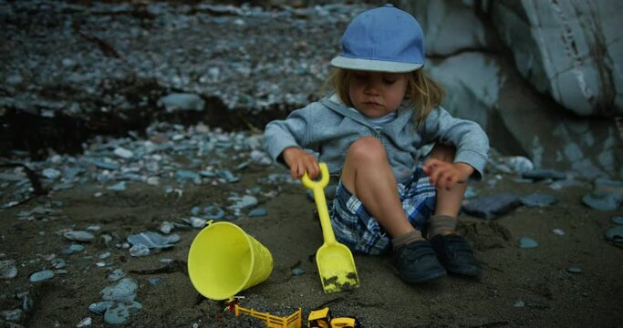 Preschooler boy playing with bucket and spade on the beach