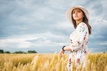 Portrait of a girl in a wheat field. Portrait of a beautiful girl in a white dress and hat on a wheat field. Girl in a white dress and hat. Wheat field. Portrait of a young woman in nature