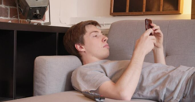 Young man plays with his mobile phone on the sofa