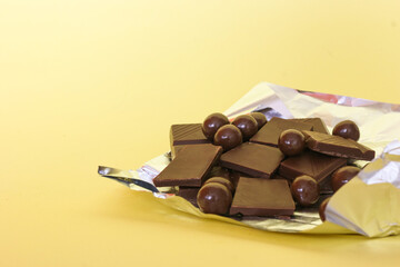close up of pieces of chocolate with chocolate balls on pckaging foil, yellow background