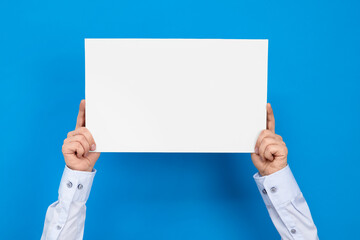 Hands hold white board on blue background with copy space for your text.