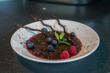 white glass plate with chocolate dessert, decorated with raspberries and blueberries and chocolate sticks
