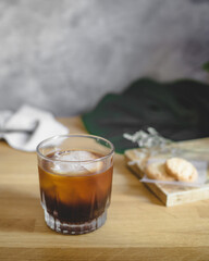 a glass of ice americano coffee with ice ball on concrete coaster and wooden table.