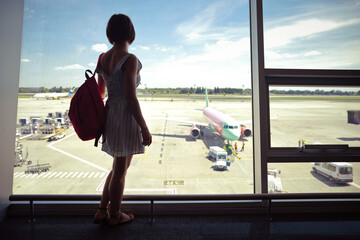 Obraz premium Caucasian woman standing inside airport and waiting her aircraft, looking through the window, airplane preparing for flight 