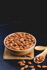almonds on dark stone table with wood spoon or scoop. Almond in wooden bowl. Nuts freely laid on dark board.