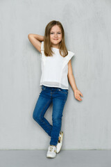 Little girl in blouse and jeans leaning to the wall in studio