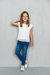 Little girl in blouse and jeans leaning to the wall in studio