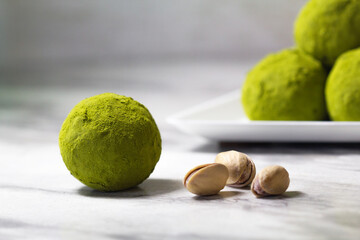 Homemade energy balls with dried apricots, raisins, dates, prunes, walnuts, pistachios and green matcha. Healthy sweet food. Energy balls in a plate on a marble grey background. Close up. Side view.