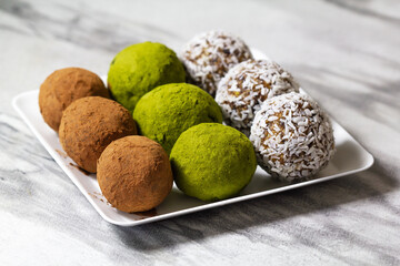 Homemade energy balls with dried apricots, raisins, dates, prunes, walnuts, pistachios, green matcha, cacao and coconut. Assortment. Healthy sweet food. Energy balls on a marble grey background.