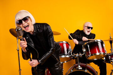 Portrait of nice attractive excited cheerful cheery grey-haired couple famous musicians playing hit single young soul having fun art isolated over bright vivid shine vibrant yellow color background