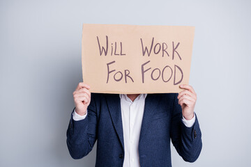 Will work for food. Photo of worker guy suffer victim financial crisis lost work hold placard search work food exchange hiding facial expression wear blue suit isolated grey background