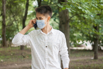 A young man in a mask talking on the phone outdoors