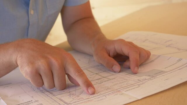 SLOW MOTION, CLOSE UP, DOF: Unrecognizable man runs his fingers along the detailed blueprints of a house under construction. Unknown architect analyses his floor plans during the construction phase.
