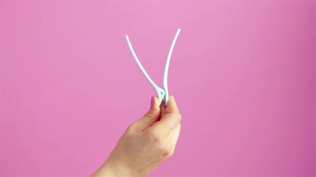 woman hand holding hair clip on pink background close up
