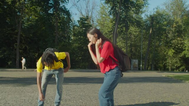 Handsome african american male student busy with smartphone bumping into attractive asian female student at university campus, being sorry and helping to collect fallen textbooks and books.