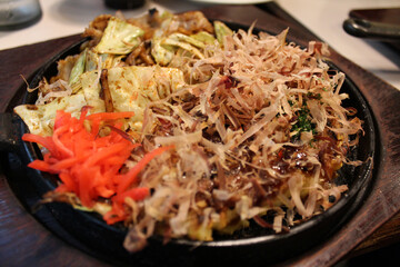 Okonomiyaki, Japanese Pizza topped with bonito flakes and sliced-pickled ginger in a hot iron frying pan in Kyoto, Japan