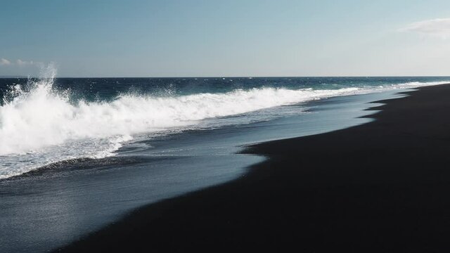 Wild beach with black volcanic sand on a sunny day.