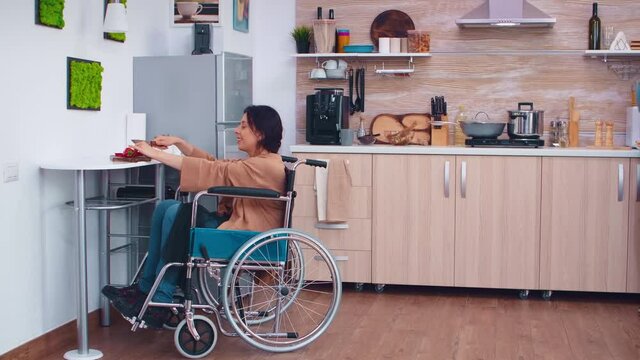 Woman with legs paralysis in wheelchair cutting red pepper on slicing board. Woman with paralysis handicap disability handicapped difficulties helping in the kitchen