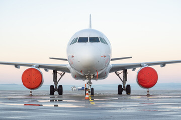 Obraz premium Front view of white airplane. Jet commercial aircraft on airport apron, morning daylight sky, puddles after rain. Modern technology in fast transportation, private business travel, charter flight.