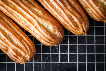 Fresh yellow toasted eclairs stacked in a pile on a pastry lattice on the black background