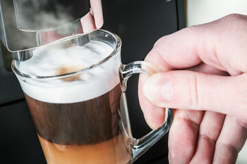 hand picks up a glass of hot cappuccino with foam made in the coffee machine