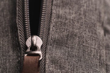 Closeup opened zippers with metal slider body with leather pull tab of gray cloth bag