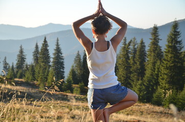 girl practices yoga at sunset in the mountains
